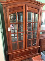 Front view of wooden petite cabinet showing glass paneled double doors and bottom drawer.