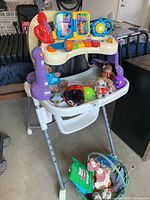 Full view of baby high chair with musical toy panel and assortment of plush toys on seat and tray.