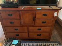 Full front view of the dresser showing its warm brown wood finish, seven black-handled drawers, and central cabinet door.