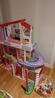 Full view of Barbie Dreamhouse showing three levels, purple slide, and blue elevator on the side, with bin of dolls and clothes nearby.