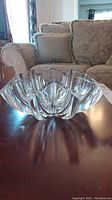 Front angle view of a heavy clear glass bowl with scalloped geometric edges on a wooden surface.