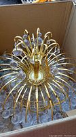 Top view of chandelier inside cardboard box showing brass arms and glass crystal accents