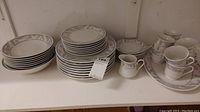 Photo showing stacks of various plates and bowls, cups and saucers arranged with a small pitcher and an oval serving plate on a shelf.