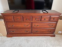 Front view of seven drawer dresser with cherry finish and metal handles, top surface with marks and scratches, TV on top for scale