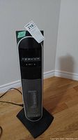 Full front view of black Bionaire tower heater on hardwood floor with tags visible.