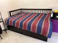Full view of IKEA dark wood day bed with striped bedding and three storage drawers visible underneath.