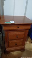 Front view of one wooden nightstand showing three drawers and top surface