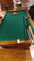 Front view of pool table with racked balls and cues on playing surface