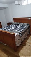 Full view of queen wood bed frame with mattress, footboard and headboard, showing bed assembled with bedding.