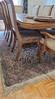 Wool area rug under dining table and chairs showing intricate floral and vine patterns with fringed edges.