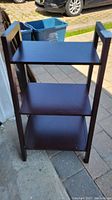 Full front view of the 3-tier dark brown wooden shelf unit on outdoor pavement showing the overall structural condition and design.