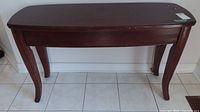 Front view of wooden table showing scratches on the surface and curved legs.