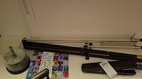 Photo showing black metal tripods/light stands, white extendable tripods, the spindle of blank CDs, and the photography book on the floor.