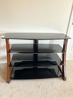 Front view of the TV and media stand showing three black tinted tempered glass shelves and curved wood side panels.