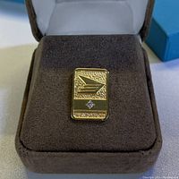 Close-up of the gold tone Birks Canada Post pin with diamond, displayed in a brown padded case.