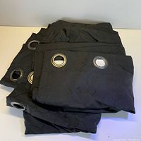 Photo of folded black curtain panels showing silver metal grommets and subtle circular pattern in fabric.