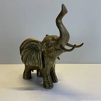 Front angled view of the brass elephant figure showing detailed ears, raised trunk, and tusks.