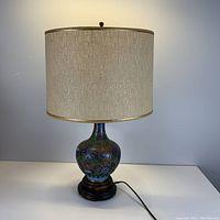 Full view of the table lamp showing colourful metal inlay body, fabric shade, wood base and power cord.