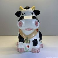 Front view of the cow cookie jar showing the full ceramic body painted with black and white spots with pink accents and floral decorations.