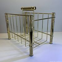 Front angle view showing gold coloured metal magazine stand with bamboo style posts and horizontal handle.