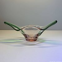Front view of the green and pink art glass stretch bowl, showing the extended green-tinted curved sides and pink base.