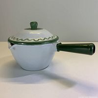 Side view of white cast iron enamel pouring pot with green handle and lid knob, showing spout and lid design.