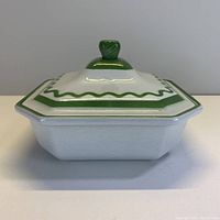 Front view of the square dish with lid showing green and white enamel decoration and leaf-shaped knob on the lid.