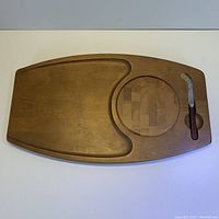 Full view of Mid Century wooden charcuterie board showing main flat surface, circular inset for detachable cutting section, and slot holding Sheffield cheese knife.