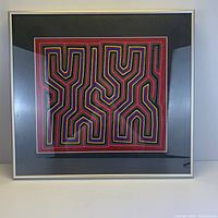Framed multicolored textile piece with geometric patterns in a silver frame.