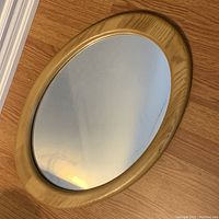 Oval mirror showing the light wood frame and full mirror surface on a wooden floor.