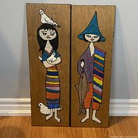 Full view of two rectangular wood panels with gravel art depicting two stylized figures each with animals or objects.