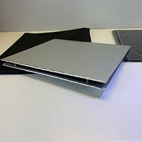 Closed silver steel art portfolio with hinge side, black soft zipper case to left and sheet protectors to right.