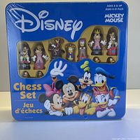 Front view of the sealed Disney chess set tin box showing themed chess pieces behind the clear window, with main characters illustrated on the box.