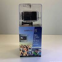 Front of Safari 5 camera in clear plastic packaging showing camera and front-facing LCD screen and key features.