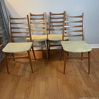 Front view of set of 4 wooden ladder back dining chairs with beige upholstered seats on wooden floor.