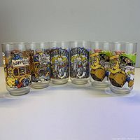 Front view of the 6 clear glasses arranged in a row showing colorful cartoon prints of Muppet characters including Miss Piggy, vintage car, and the Happiness Hotel.