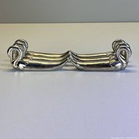 Two swan-shaped silver-colored utensil rests positioned facing each other, showing side profile and detailing of the swan heads and bodies.