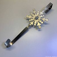 Photo showing the snowflake detail and hook of the stainless steel door holder on a white background.