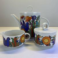 Full set photo including teapot, creamer, and sugar bowl with vibrant multicolor flower and bird patterns on white porcelain.