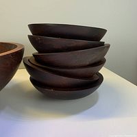 Stack of twelve small dark brown wooden bowls showing minor chips and wear on edges