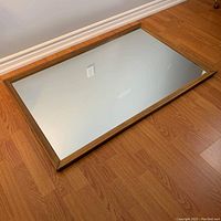 Top-down photo showing reflective glass surface and wooden frame on a hardwood floor.