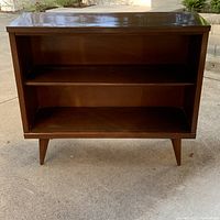 Front view of the wooden mid century display cabinet showing two shelves and tapered legs.