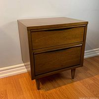 Full view front angle of the vintage side table showing two drawers and tapered legs on wood flooring.