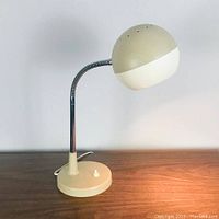 View of vintage desk lamp on wooden surface showing adjustable round head and base with push button switch.