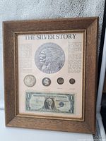 Framed display showing the entire "The Silver Story" currency collection with coin images, physical coins, silver granules, and a $1 silver certificate in a wooden frame.