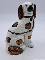 Front view of white ceramic dog with copper patches, ears, tail, and chain detail.