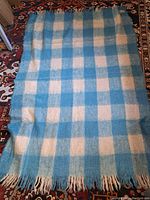 Full view of the blue and off-white checkered mohair blanket with fringed edges laid out flat.