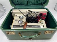 Kenmore sewing machine inside green hard carrying case with lid open. Showing machine body, power cord, and foot pedal.