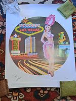 Full view of Las Vegas poster print in circular design, showing showgirl, iconic signage, and street, on white backing paper.