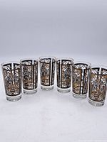 Front row photo showing the full set of six glasses with consistent floral decorative panels in gold and black and gold rims.